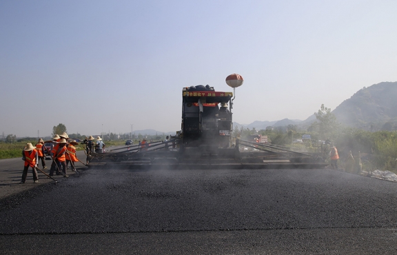 2019年8月，宜春經(jīng)開區(qū)S311路面攤鋪現(xiàn)場，工友們輔助路面兩側(cè)的分料、補(bǔ)窩等作業(yè)